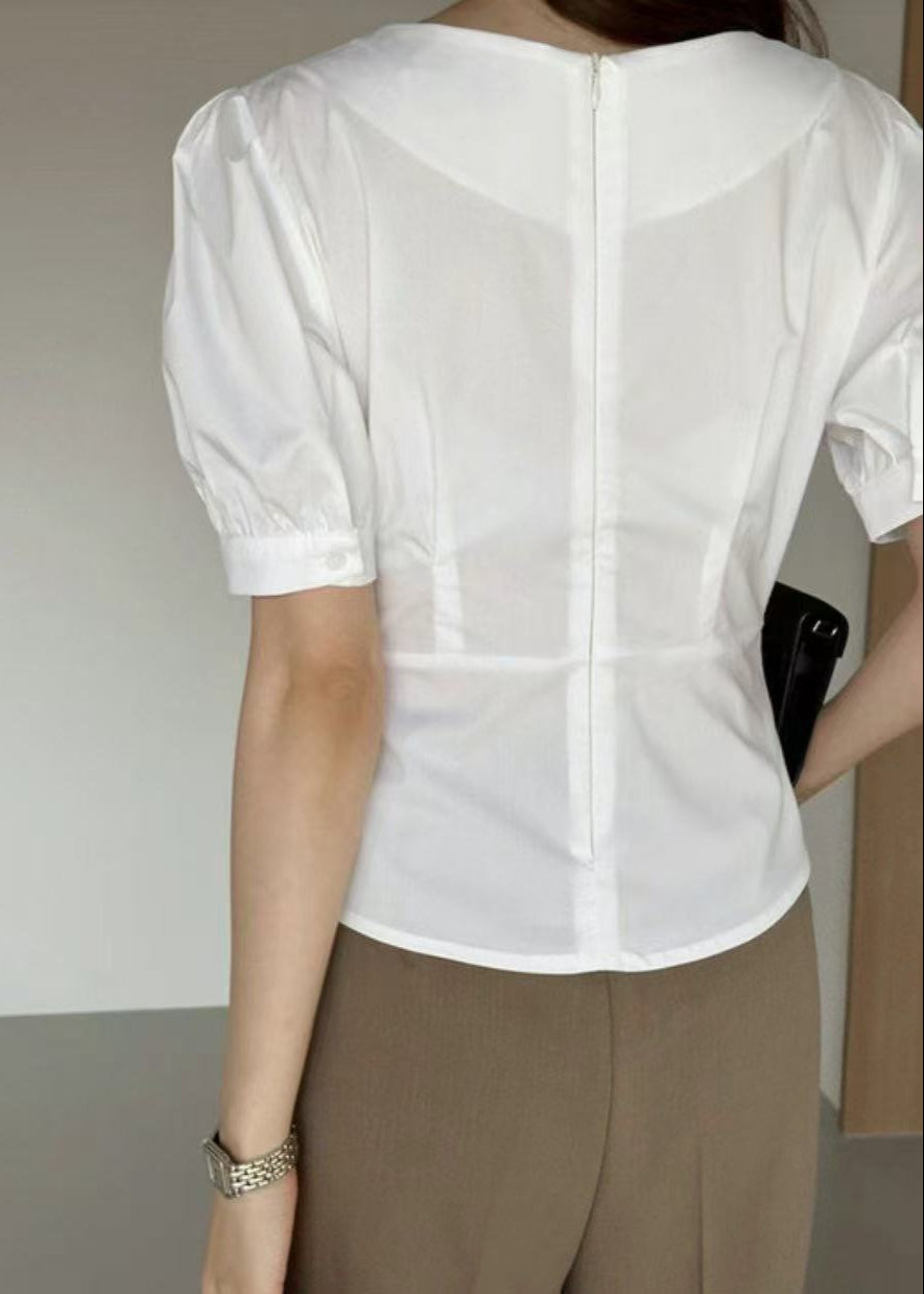 Person wearing a white blouse and brown pants against a plain background