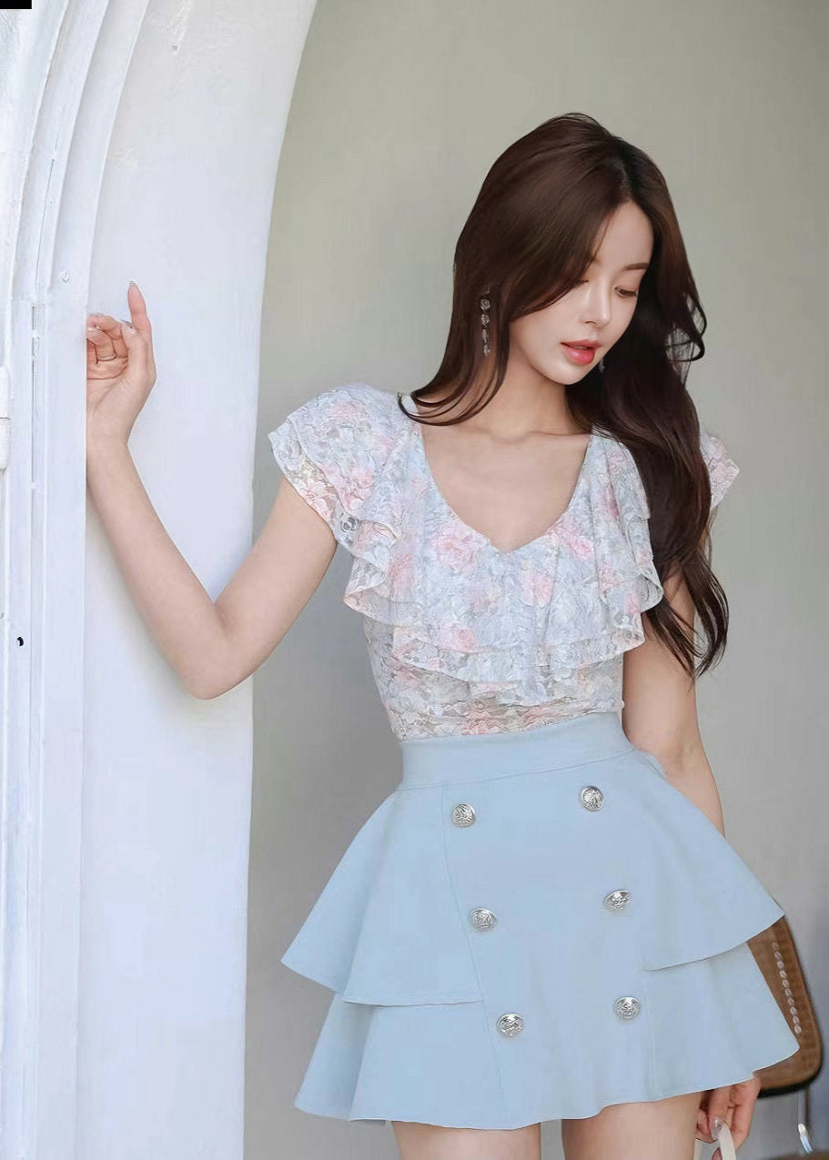 Woman wearing a light blue floral top and skirt with buttons.