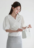 Woman wearing a white blouse and plaid skirt holding a handbag against a white background